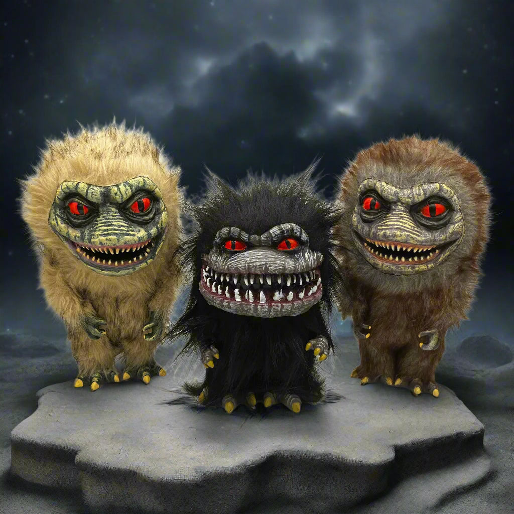 Three Critters movie monsters with red eyes and sharp teeth standing on a rock under a dark sky.