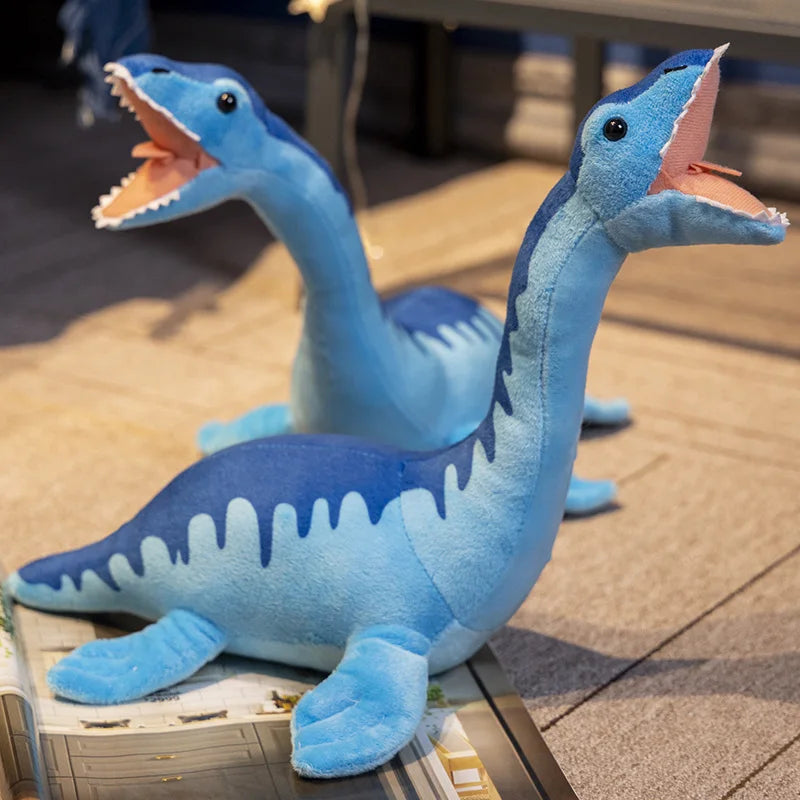 Two blue Loch Ness Monster plush toys with open mouths posed playfully on a magazine and carpeted floor