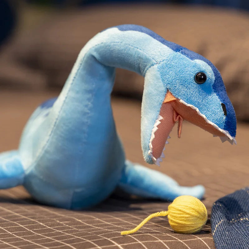 Loch Ness Monster plush toy with soft blue fabric, open mouth, and playful yellow yarn ball on a bed