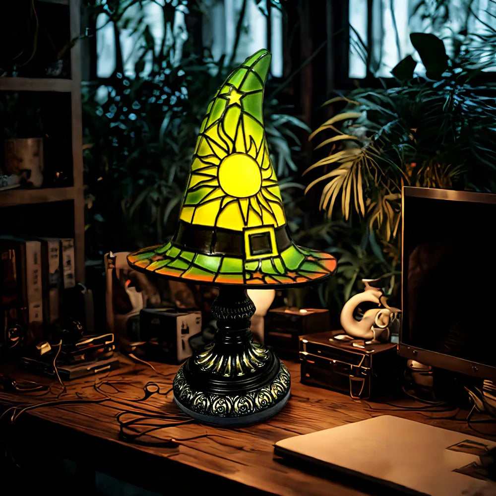 Glowing green and yellow stained glass witch hat lamp casting light on a desk in a forest-like study.