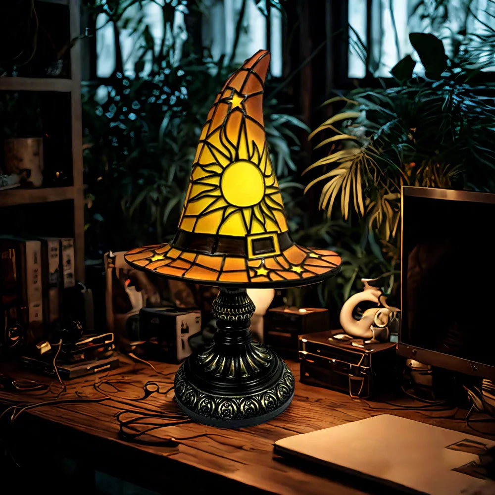 Stained glass witch hat lamp in warm orange tones glowing on a cozy wooden desk.