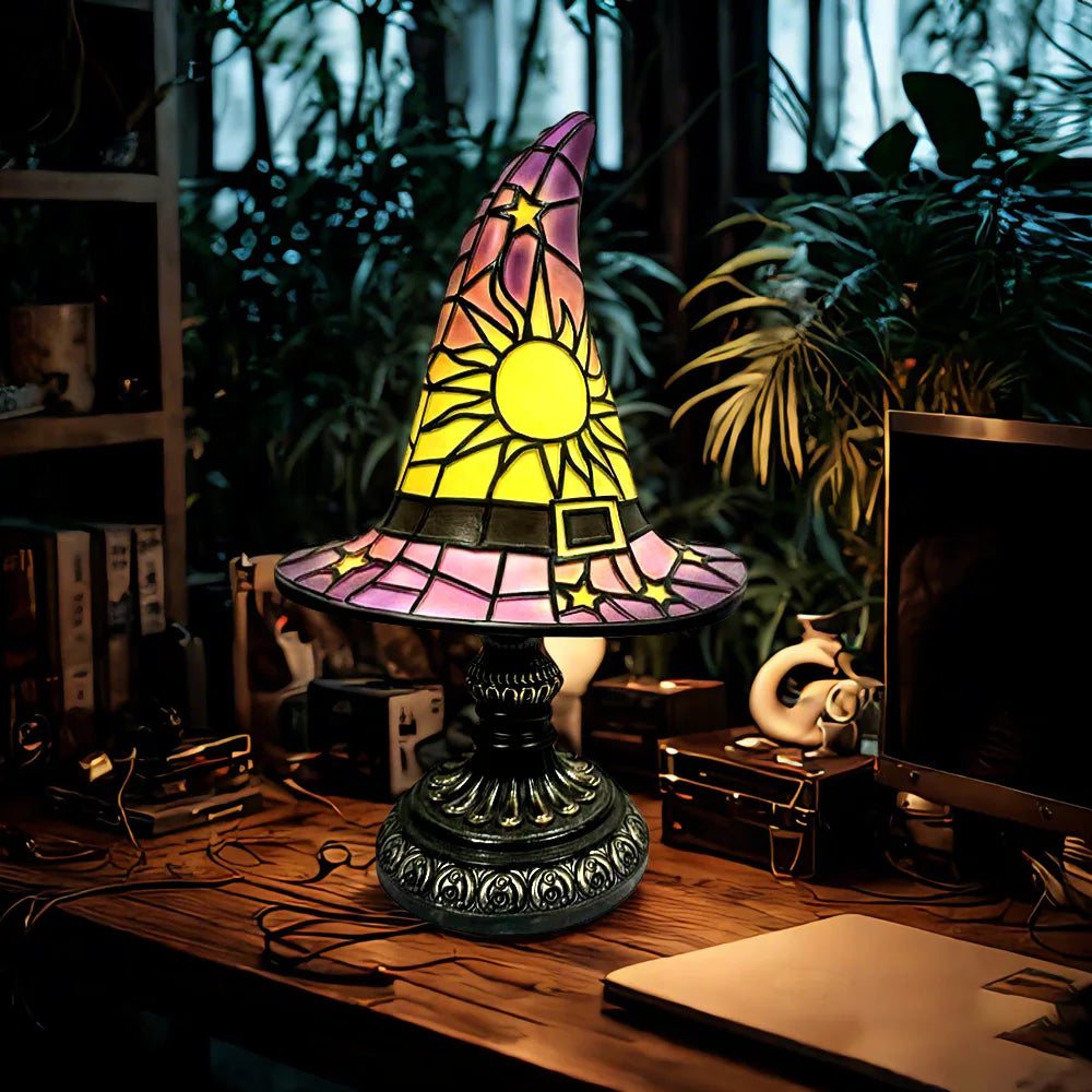 Whimsical stained glass witch hat lamp in purple and yellow, lit on a mystical desk setup