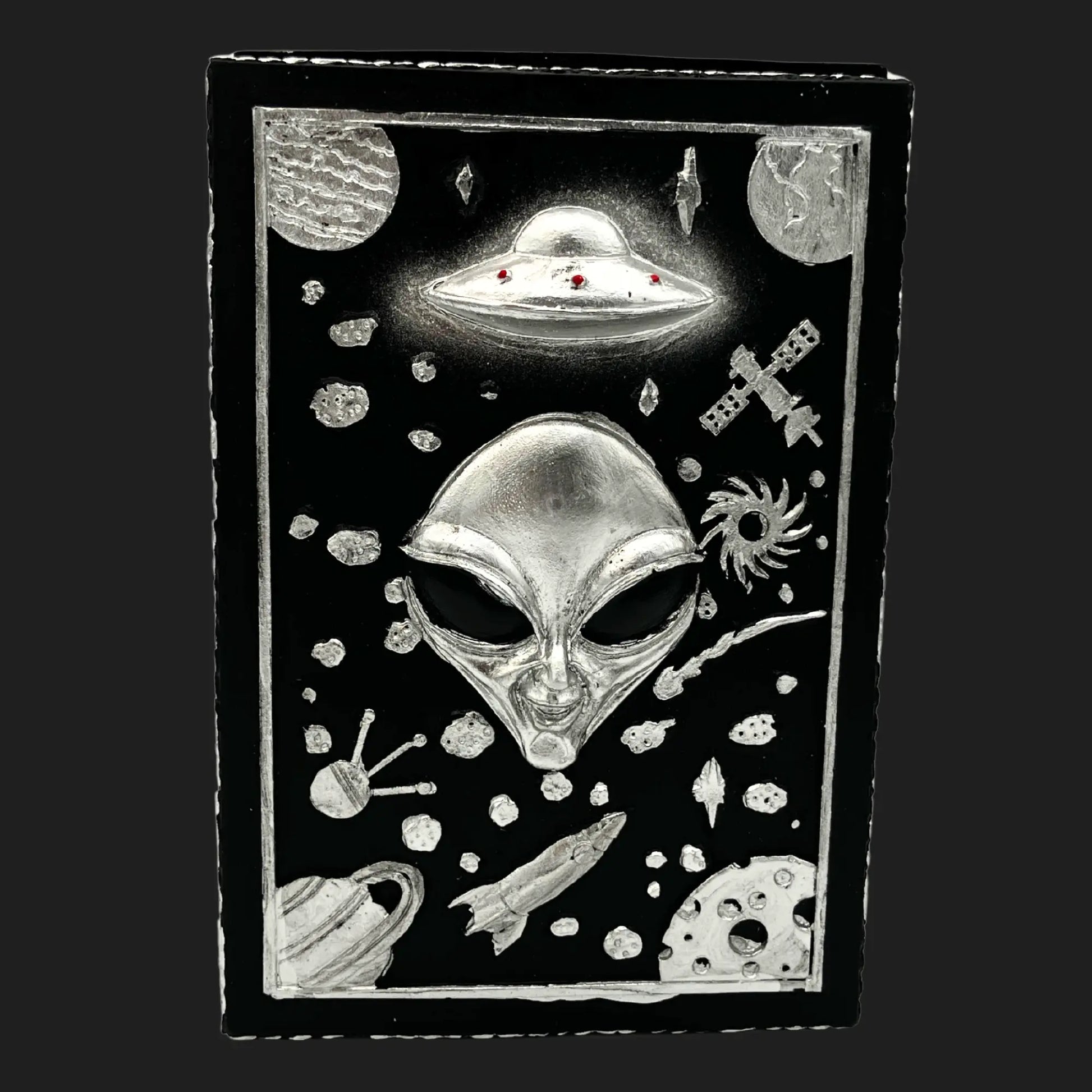 Alien trinket box lid with extraterrestrial face, UFO, planets, rockets, and galaxy designs in silver on black