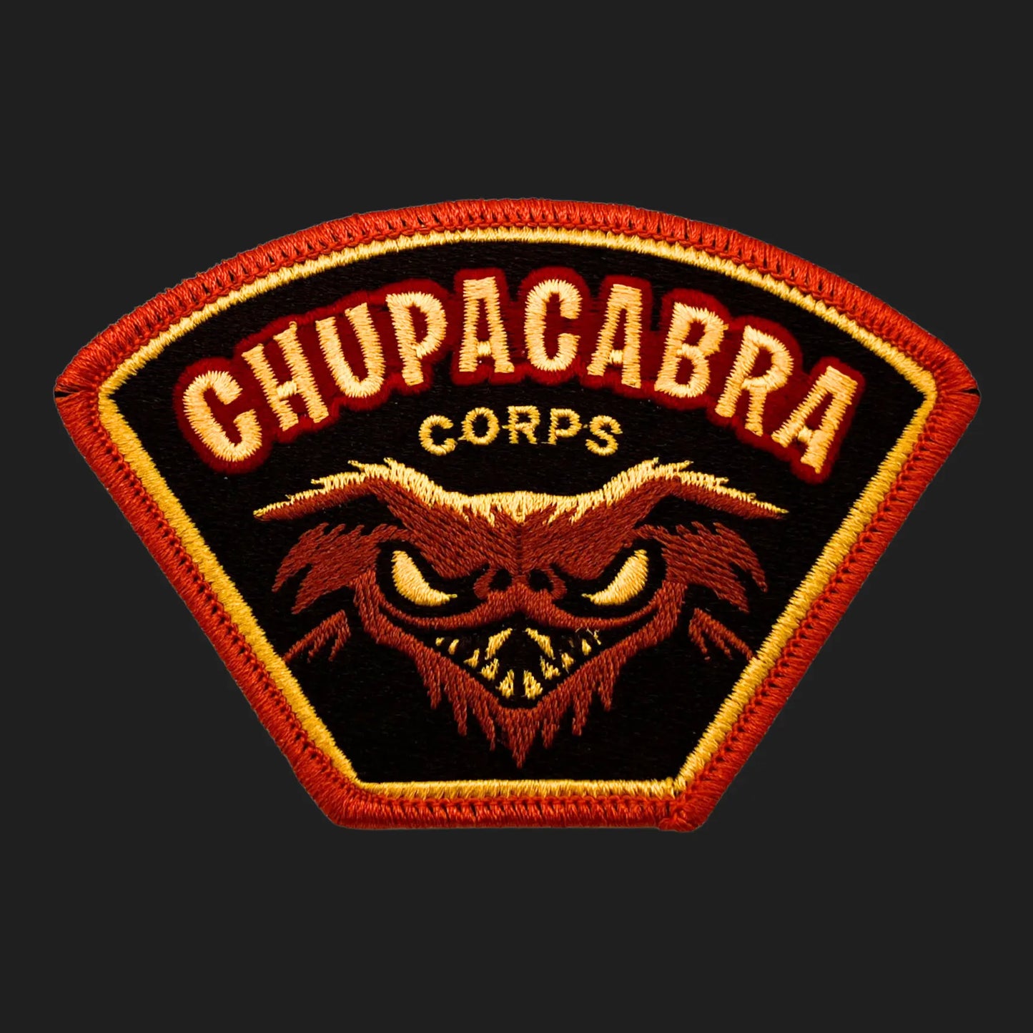 Embroidered Chupacabra Corps iron-on patch, 4 x 2.75 inches, featuring snarling goat-sucker cryptid face in red and gold.
