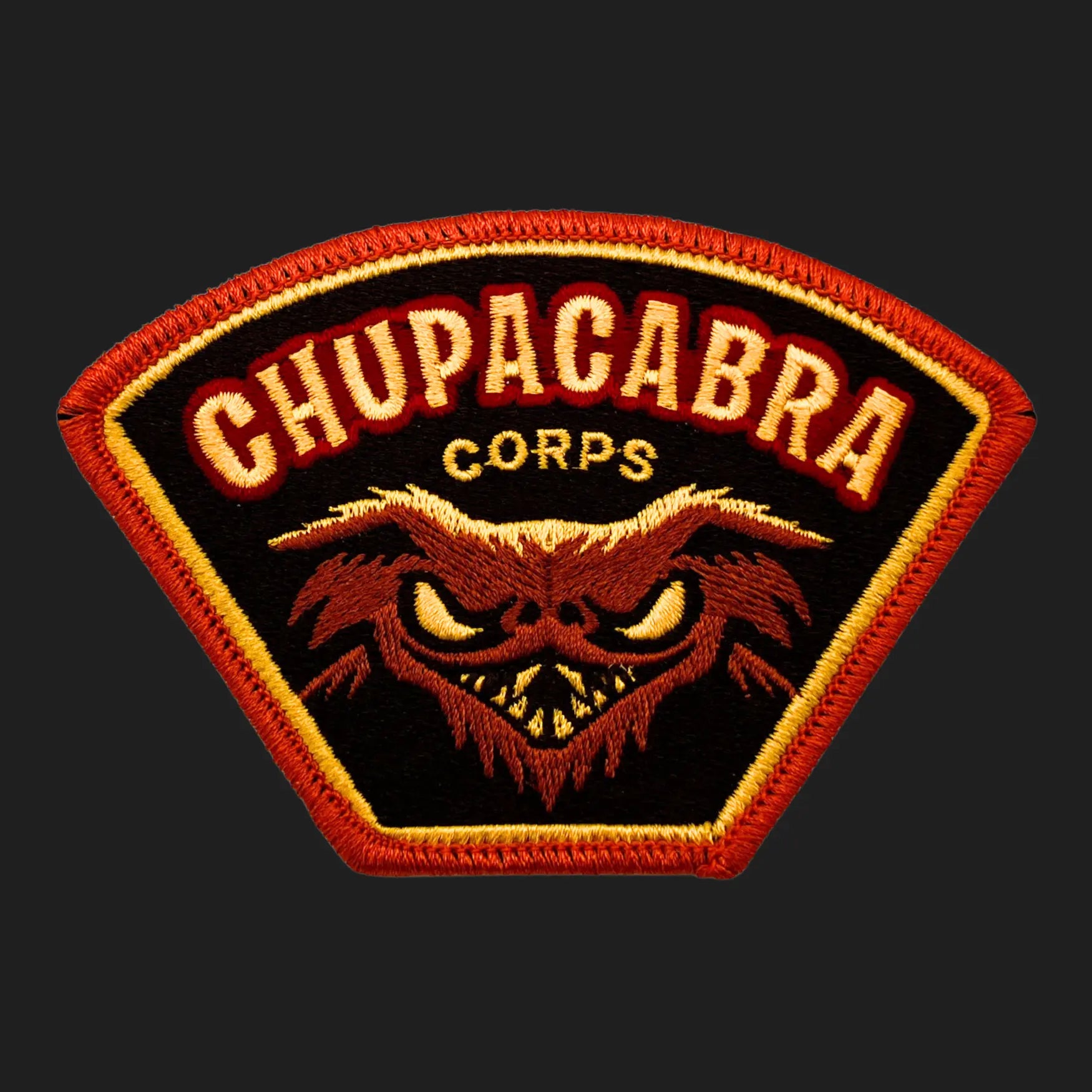 Embroidered Chupacabra Corps iron-on patch, 4 x 2.75 inches, featuring snarling goat-sucker cryptid face in red and gold.
