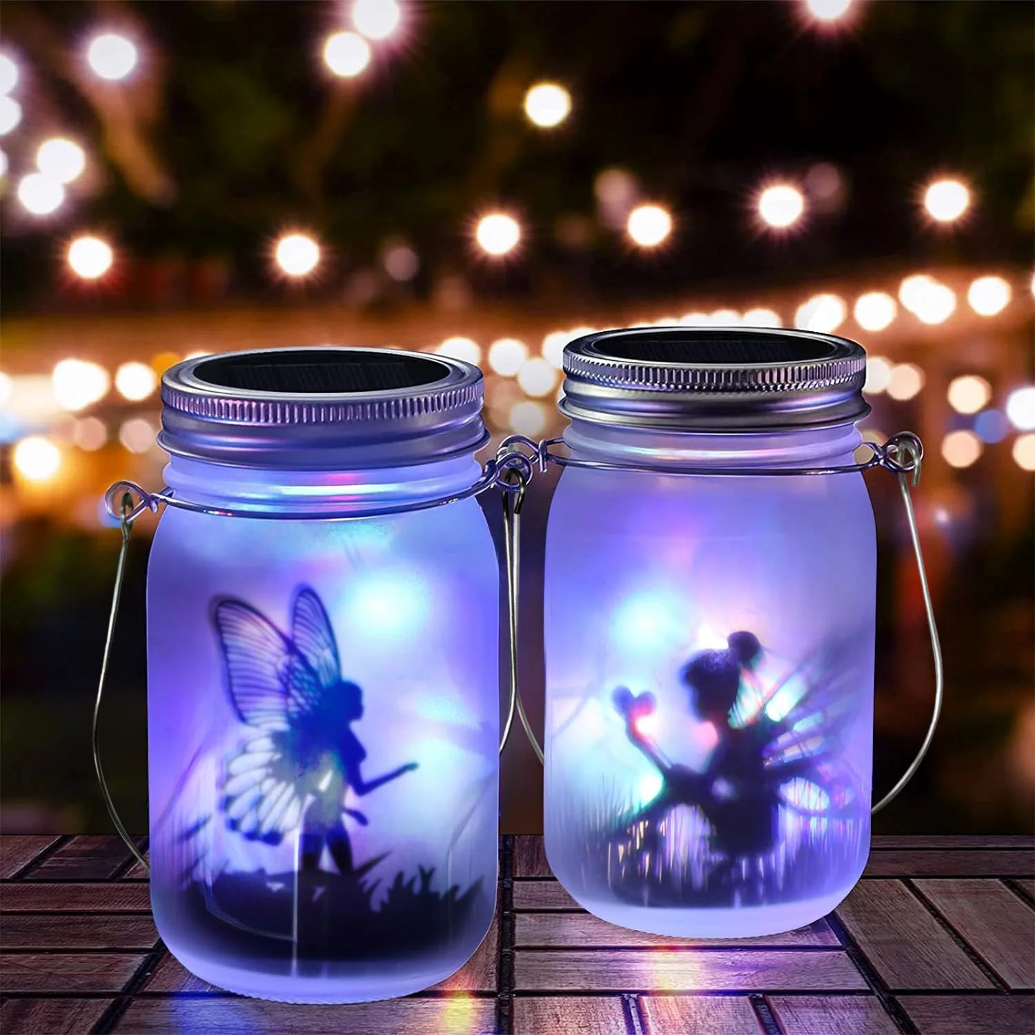 Pair of frosted solar mason jar lanterns with glowing fairy silhouettes and multicolor lights on wooden table