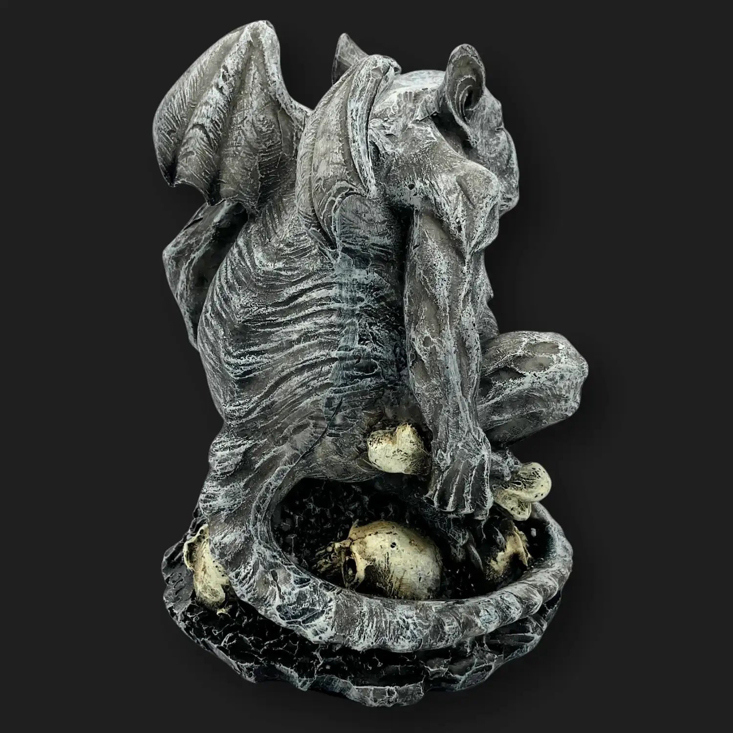 Angled view of gothic gargoyle statue with wings and skull base.
