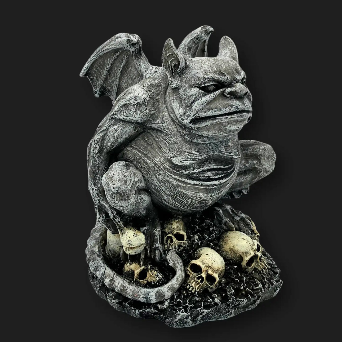 Side angle of gothic gargoyle statue perched on skulls, stone-like resin décor.