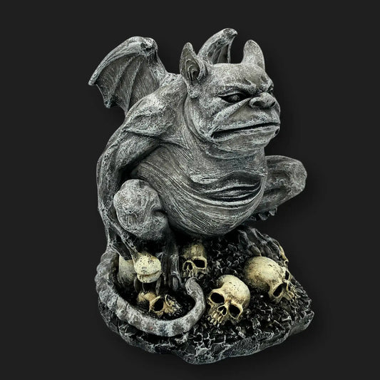 Side angle of gothic gargoyle statue perched on skulls, stone-like resin décor.