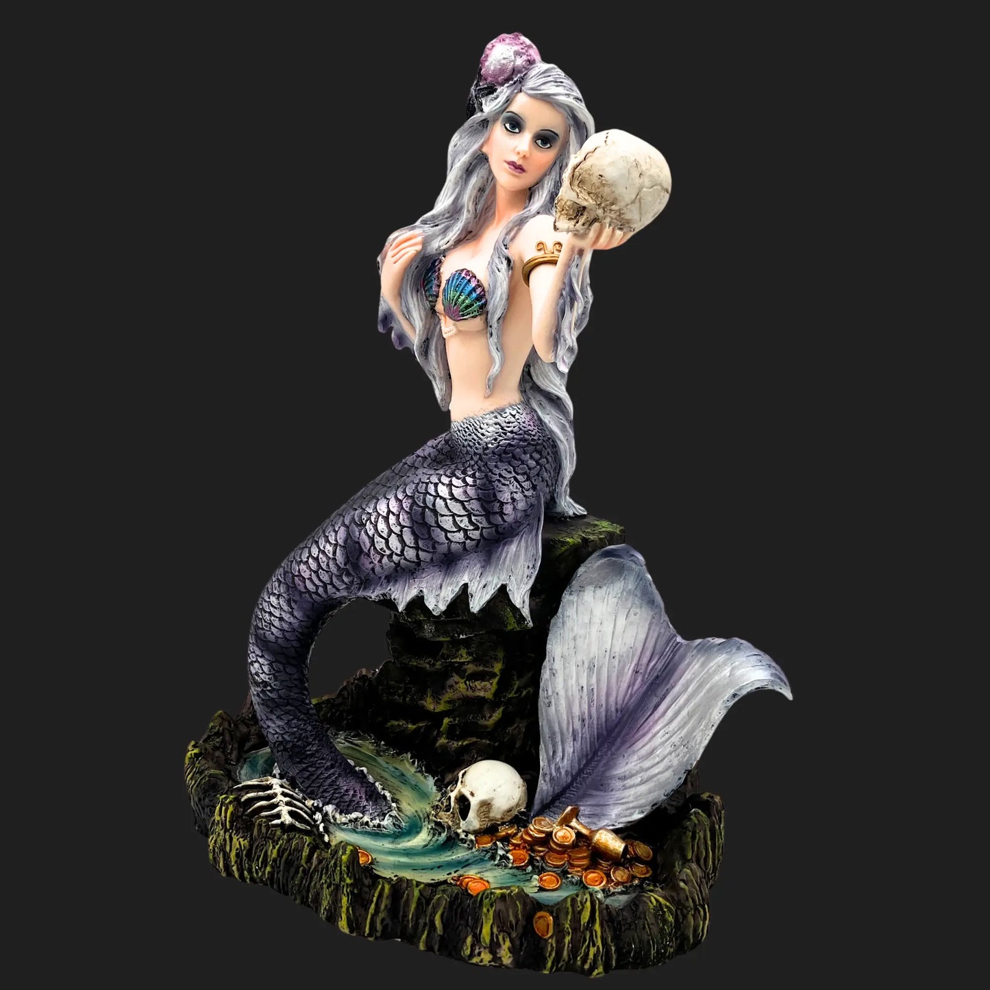Side view of gothic mermaid figurine, detailed tail and skull in hand, resting on ocean rock
