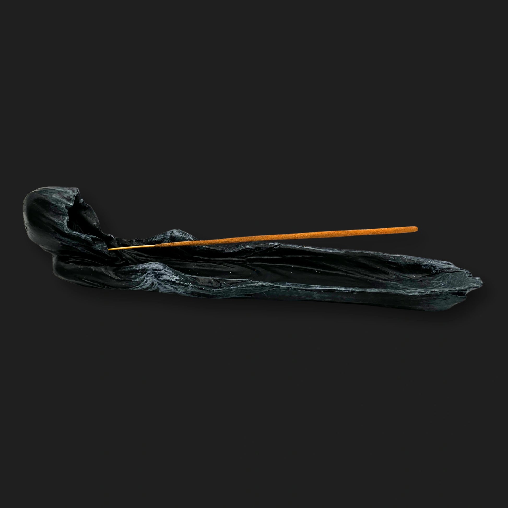 Side view of a black Grim Reaper incense holder with a hooded figure holding a stick of incense.