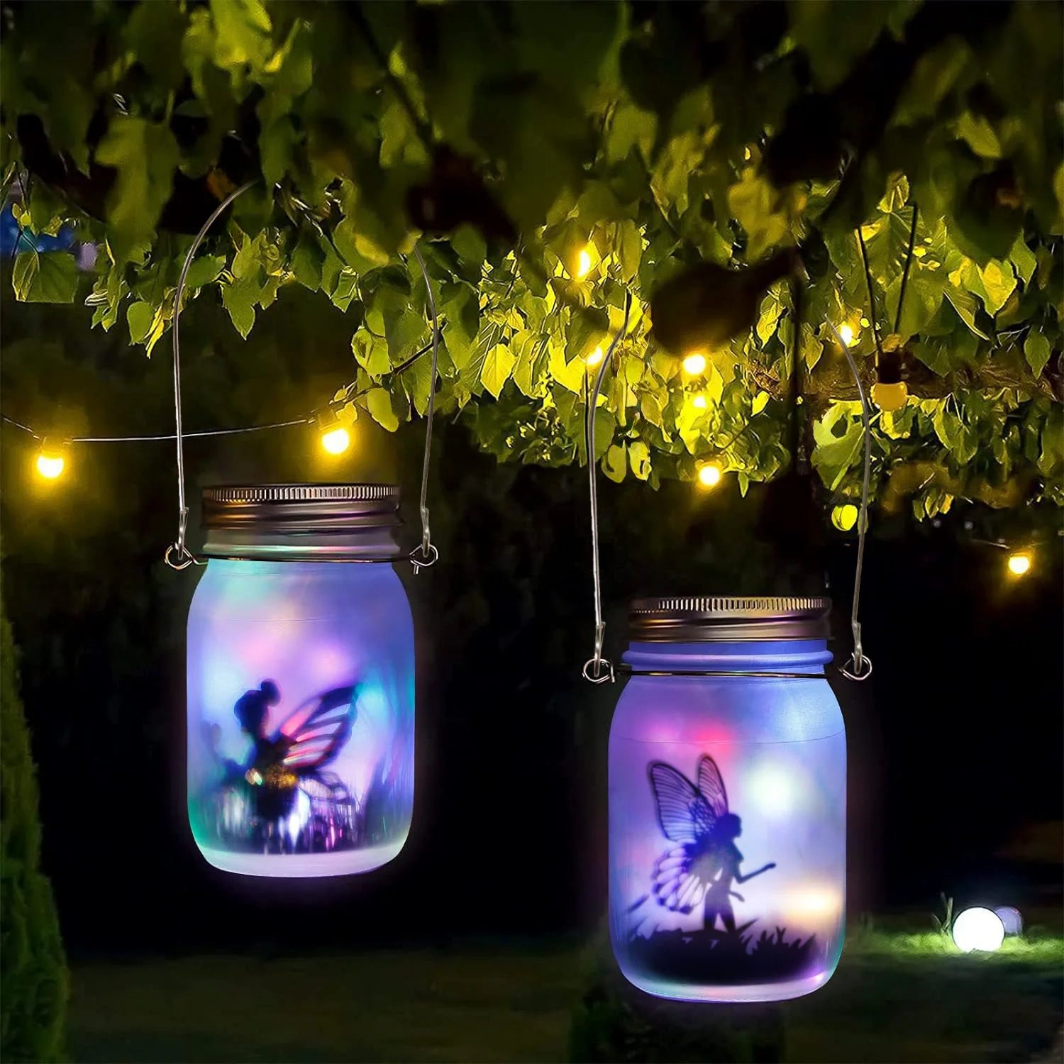 Colorful LED fairy lanterns hanging from a tree branch at night with warm garden string lights in background
