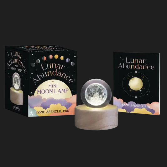 Lunar Abundance mini moon lamp glowing on wooden base with guidebook
