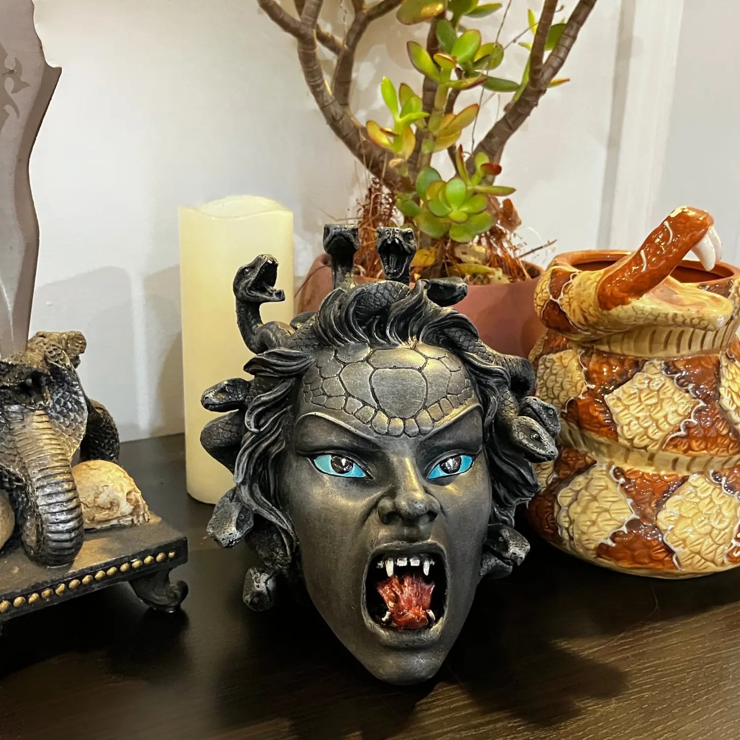 Medusa Head Sculpture Home Display – Decorative Medusa bust with snake hair, glowing eyes, and open mouth, styled on a shelf with serpent-themed décor.