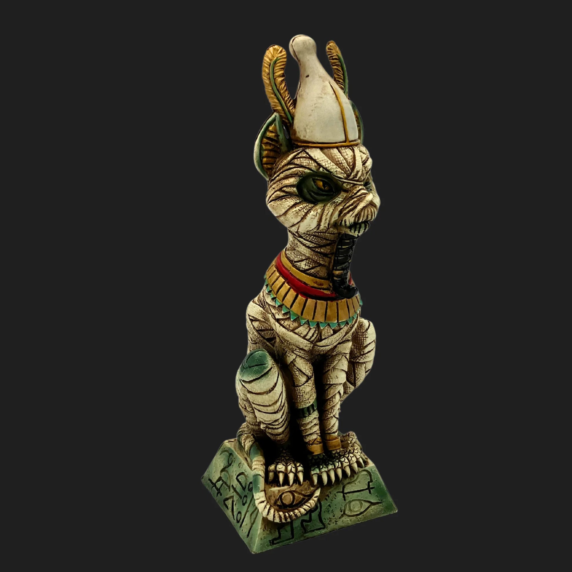 Front view of mummified Egyptian cat Osiris statue with crown, green eyes, and ornate base marked with hieroglyphs — ancient guardian figurine.