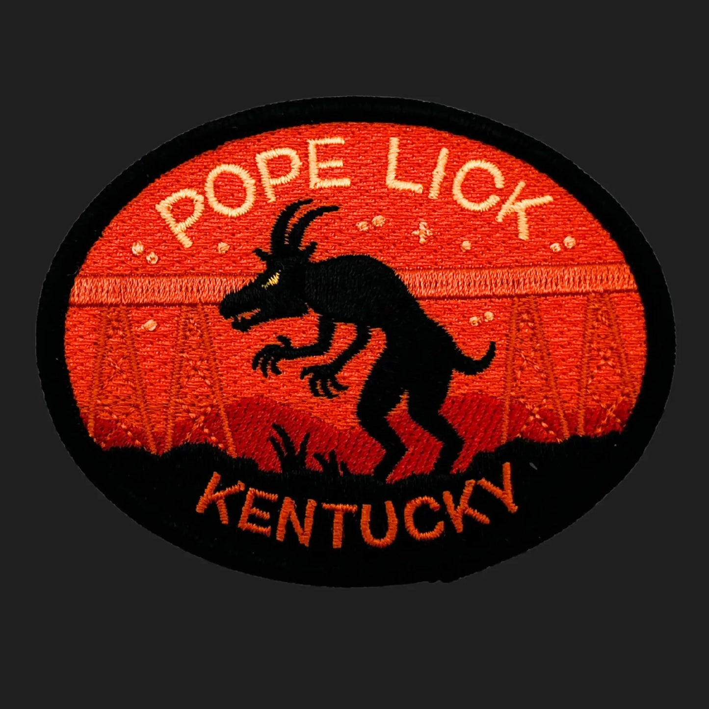 Embroidered patch featuring the Pope Lick Monster of Kentucky — a black goat-like creature silhouetted against a red sunset backdrop with a trestle bridge in the distance, text reading “POPE LICK” and “KENTUCKY.”