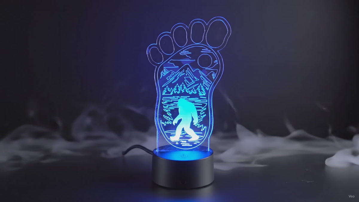 Bigfoot footprint LED lamp cycling through multiple colors with etched mountain, forest, and Sasquatch design.