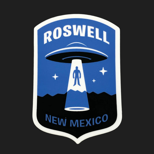 Roswell UFO sticker in blue showing flying saucer beaming up a figure over New Mexico desert