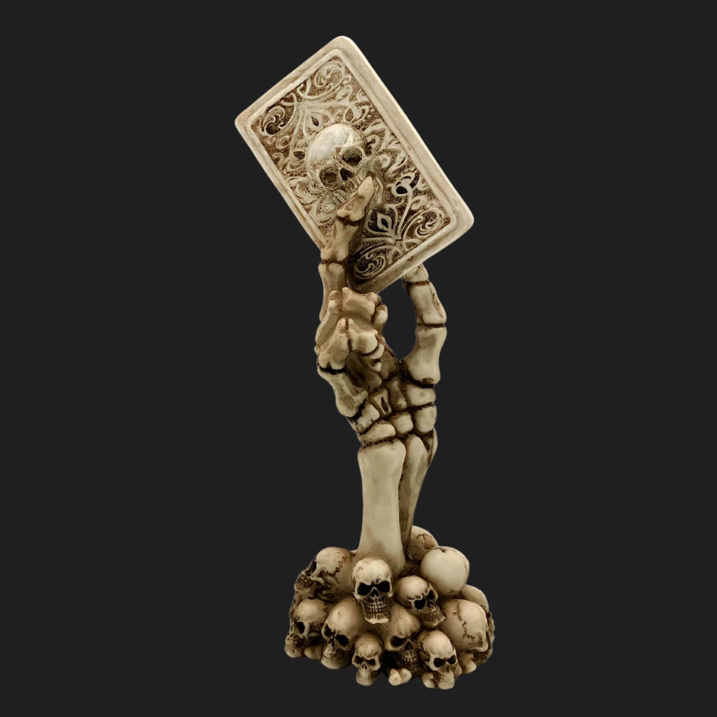 Skeleton hand statue rising from skull base holding ornate card with skull design