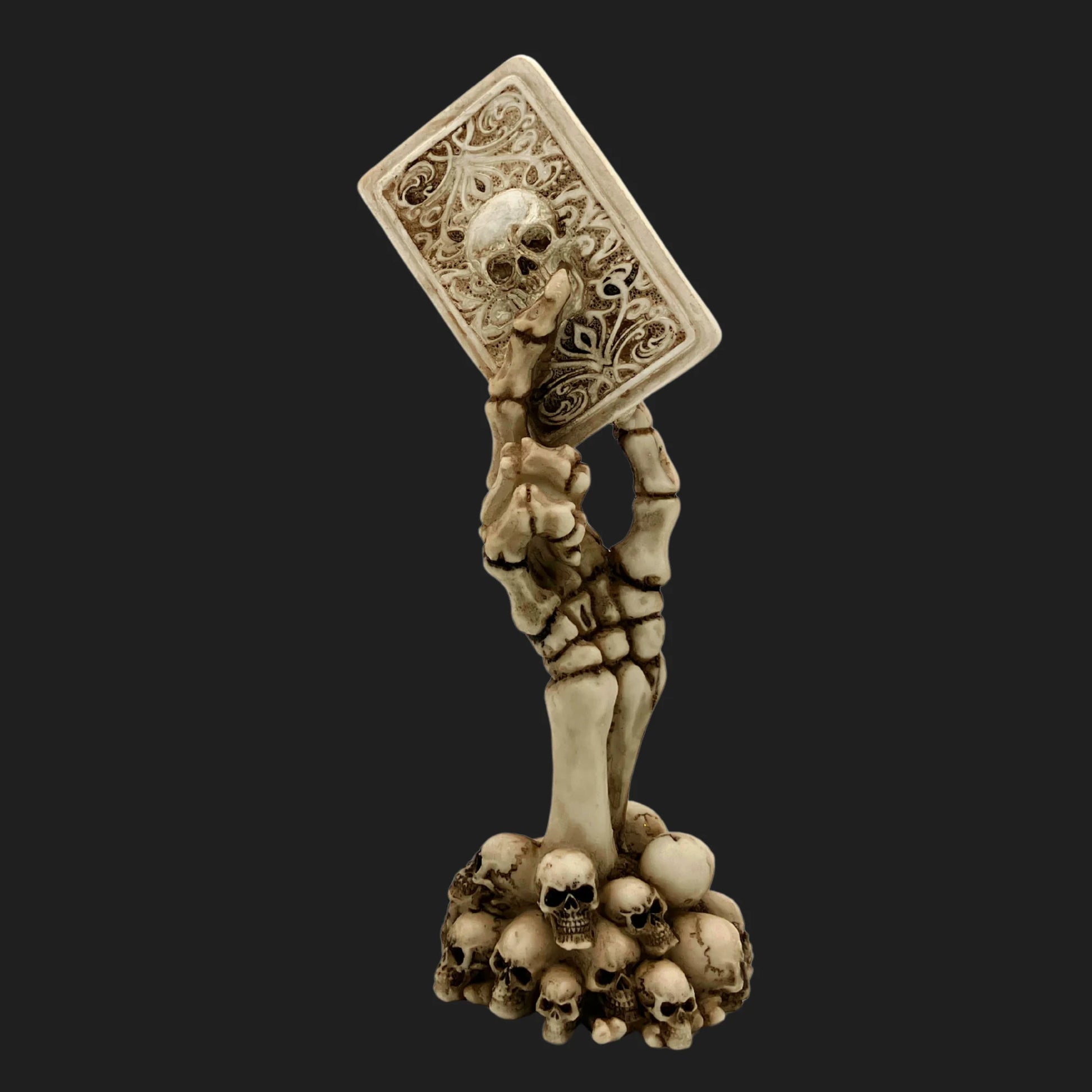 Skeleton hand statue rising from skull base holding ornate card with skull design