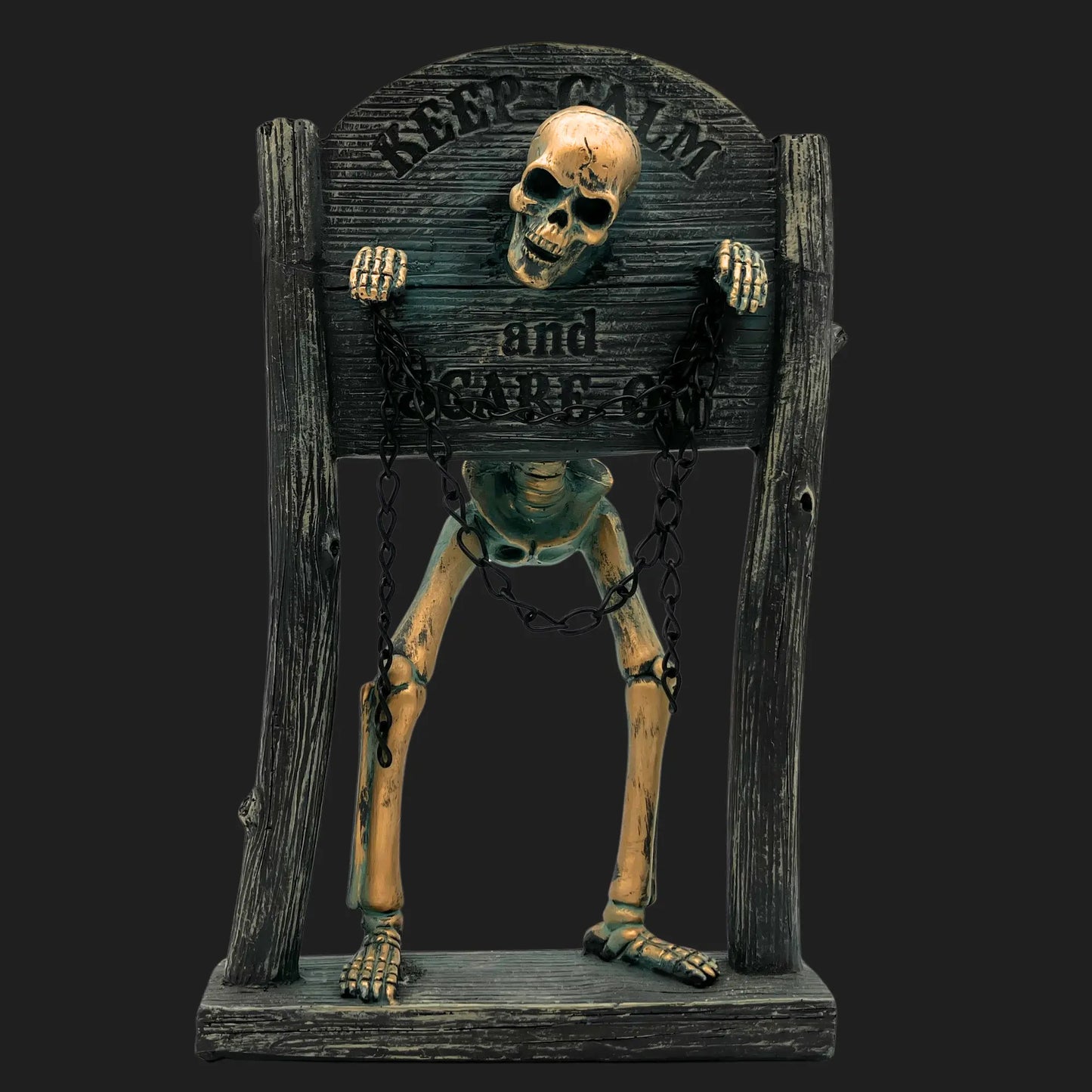 Skeleton statue in wooden stocks with chains, engraved with 'Keep Calm and Scare On'
