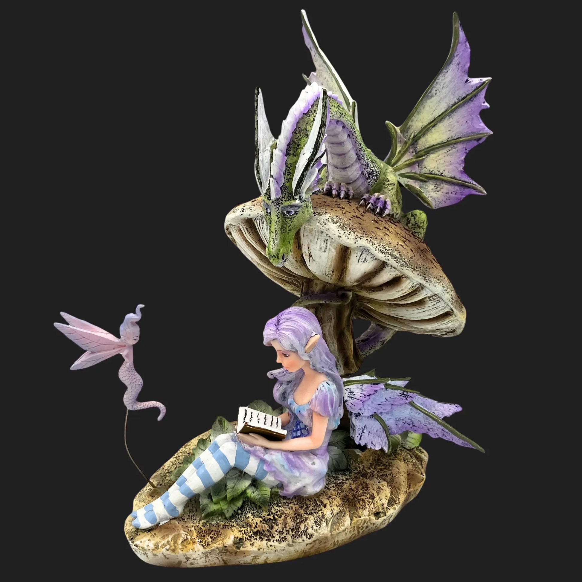 Storykeeper fairy figurine sitting under a mushroom, reading a book, with a green dragon perched above and a small sprite nearby.