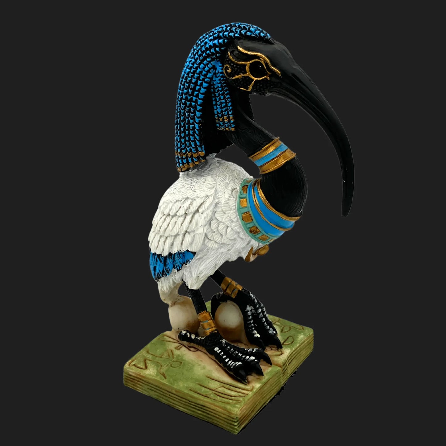 Thoth ibis-headed Egyptian god statue with ornate blue headdress, golden jewelry, and skull at feet — ancient deity figurine on engraved base.