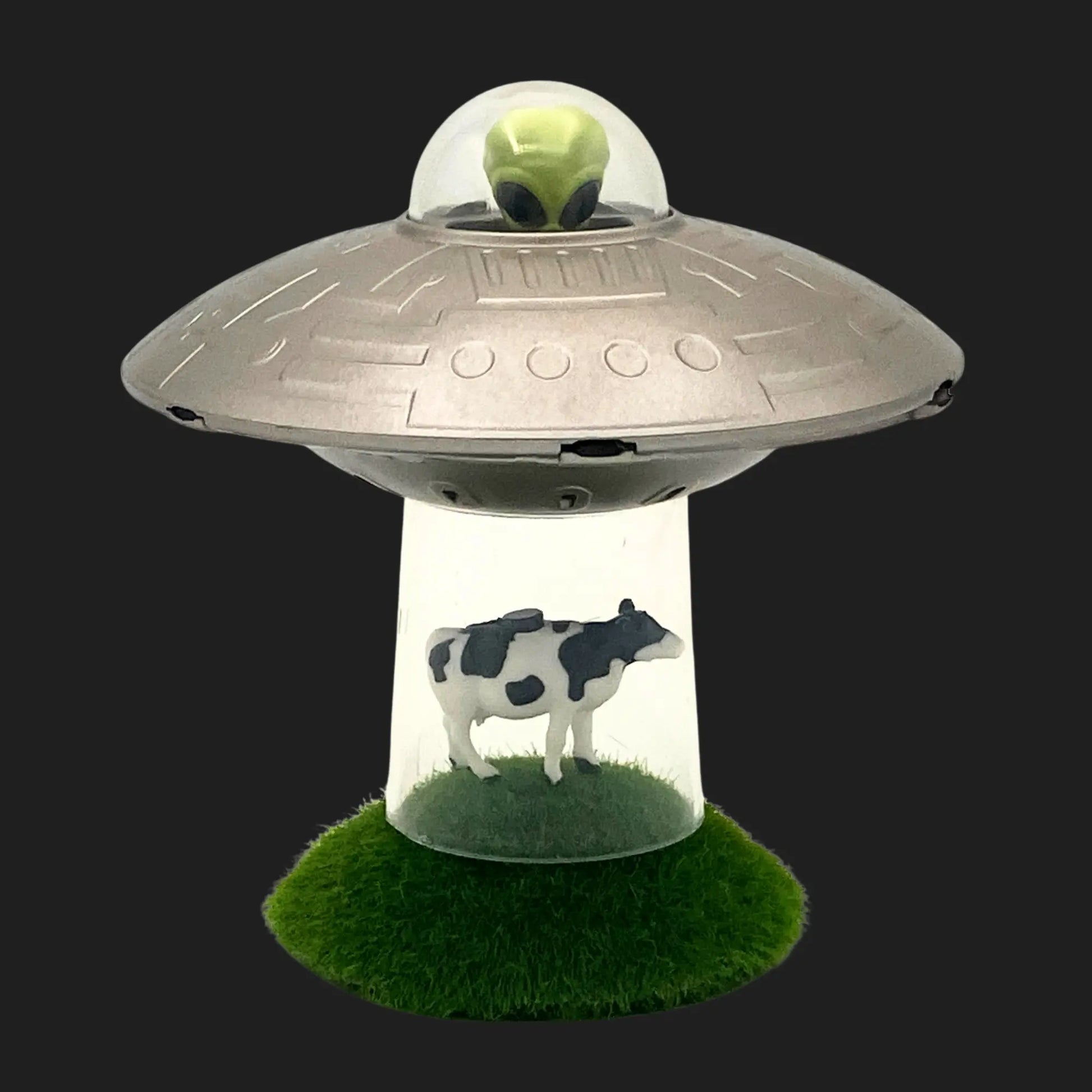 Mini UFO toy with alien pilot abducting cow figurine on grass base