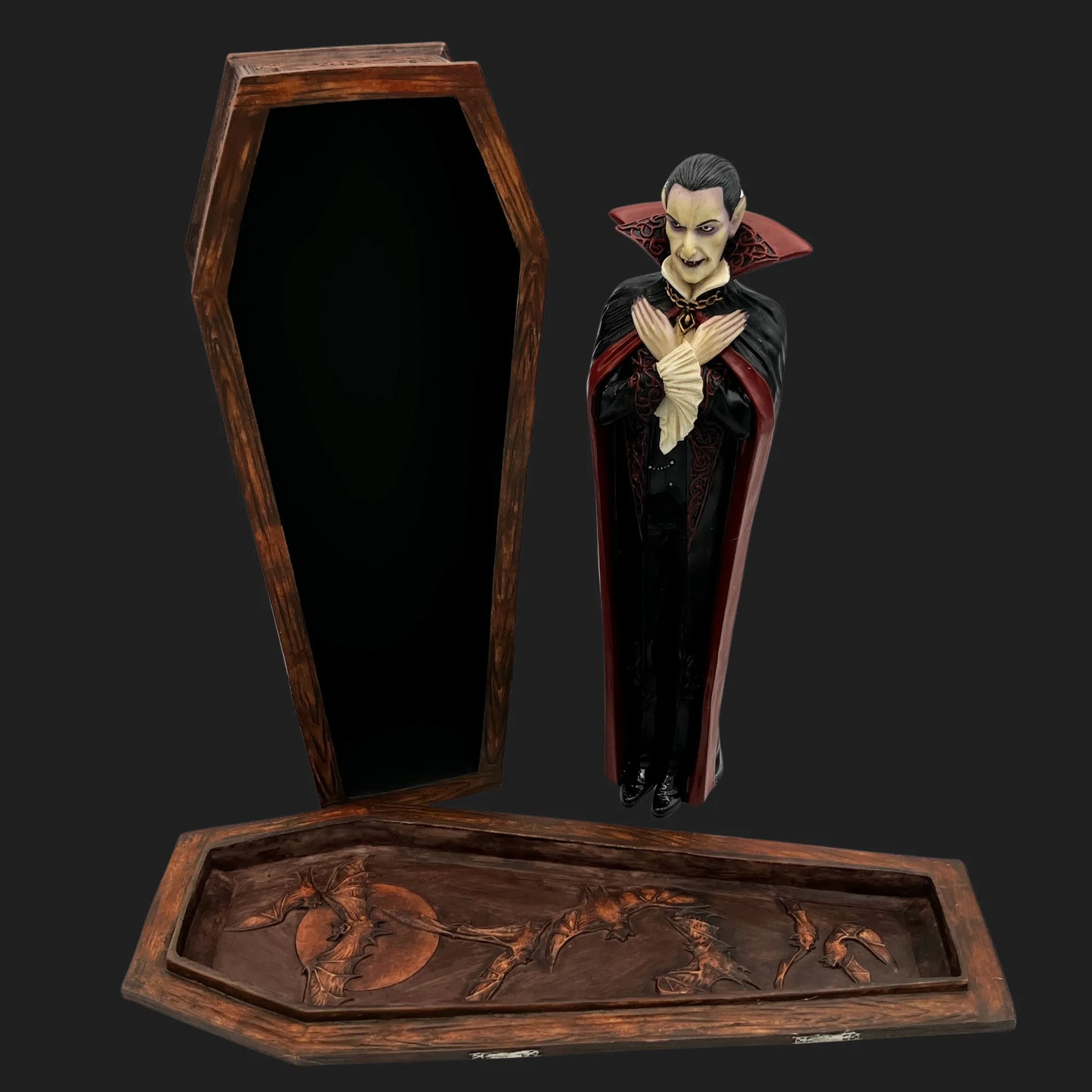 Gothic vampire figurine standing beside open wooden coffin with bat carvings