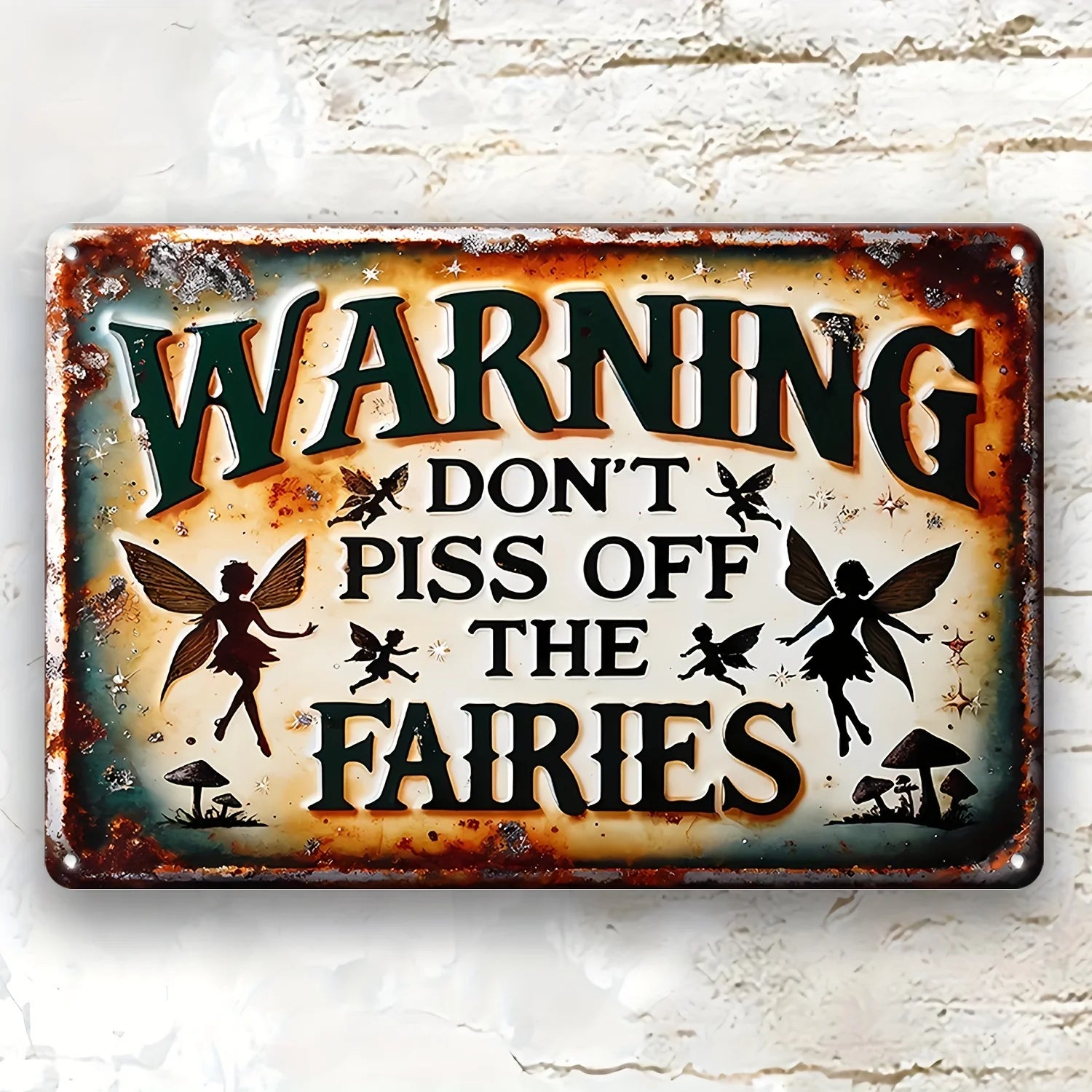 Metal sign reading “WARNING: Don’t Piss Off the Fairies” displayed on whitewashed brick wall with distressed edges and fairy silhouettes